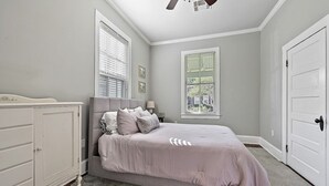 Une chambre à coucher comprenant un lit, une commode, un ventilateur de plafond et deux fenêtres.
