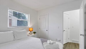 Een keurig opgemaakt slaapkamer met een bed, een bedlampje, een deur en een raam met jaloezieën.