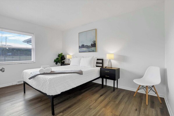 Ein Schlafzimmer mit Bett, Nachttischlampen, einem Sessel und einem Bild an der Wand.