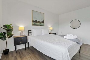 Ein ordentlich eingerichtetes Schlafzimmer mit einem Bett, Nachttischen, einer Topfpflanze und einem Bild an der Wand.
