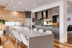 A modern kitchen with a central island, stainless steel appliances, and a wooden accent wall. - Point Haven Solar Pool, Basketball Court & Views (Mount Martha)