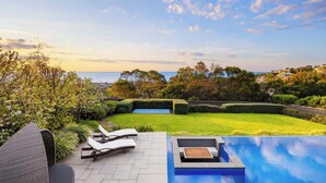 A pool area with lounge chairs, a well-manicured lawn, and a view of the sea. - Point Haven Solar Pool, Basketball Court & Views (Mount Martha)