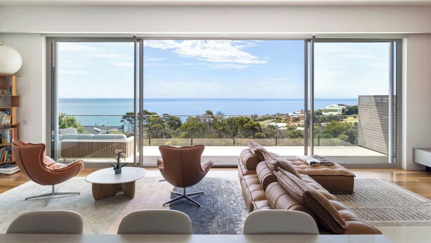 A modern living room with a large sliding glass door leading to a balcony with a view of the sea. - Point Haven Solar Pool, Basketball Court & Views (Mount Martha)