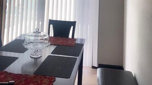 Een eetgedeelte met een tafel gedekt voor twee personen, een stoel en een raam met jaloezieën.
