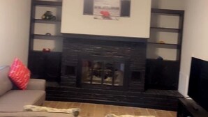 Een woonkamer met een donkere open haard, een plafondventilator en een televisie op een standaard.