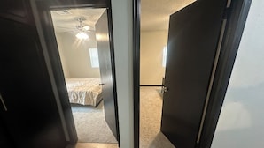 Een kamer met een bed, een plafondventilator en een deur naar een andere kamer.