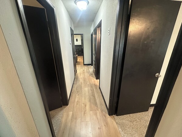 A narrow hallway with wooden flooring and black doors.