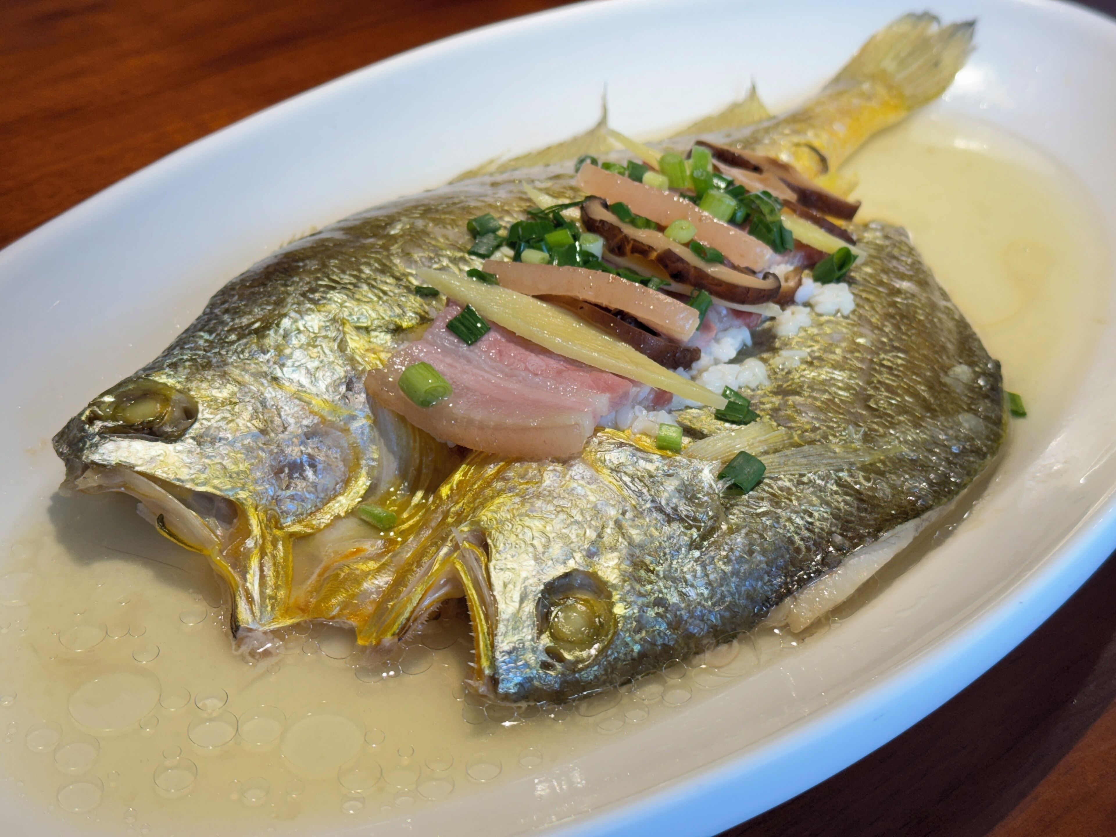 Pescado entero con carne en rodajas y guarniciones sobre un plato.