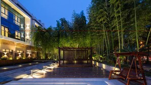 A modern building with a glass facade, a wooden pergola, and a swing set in a landscaped garden at dusk. - SSAW Boutique Hotel Shanghai South Xuhui (Shanghai)