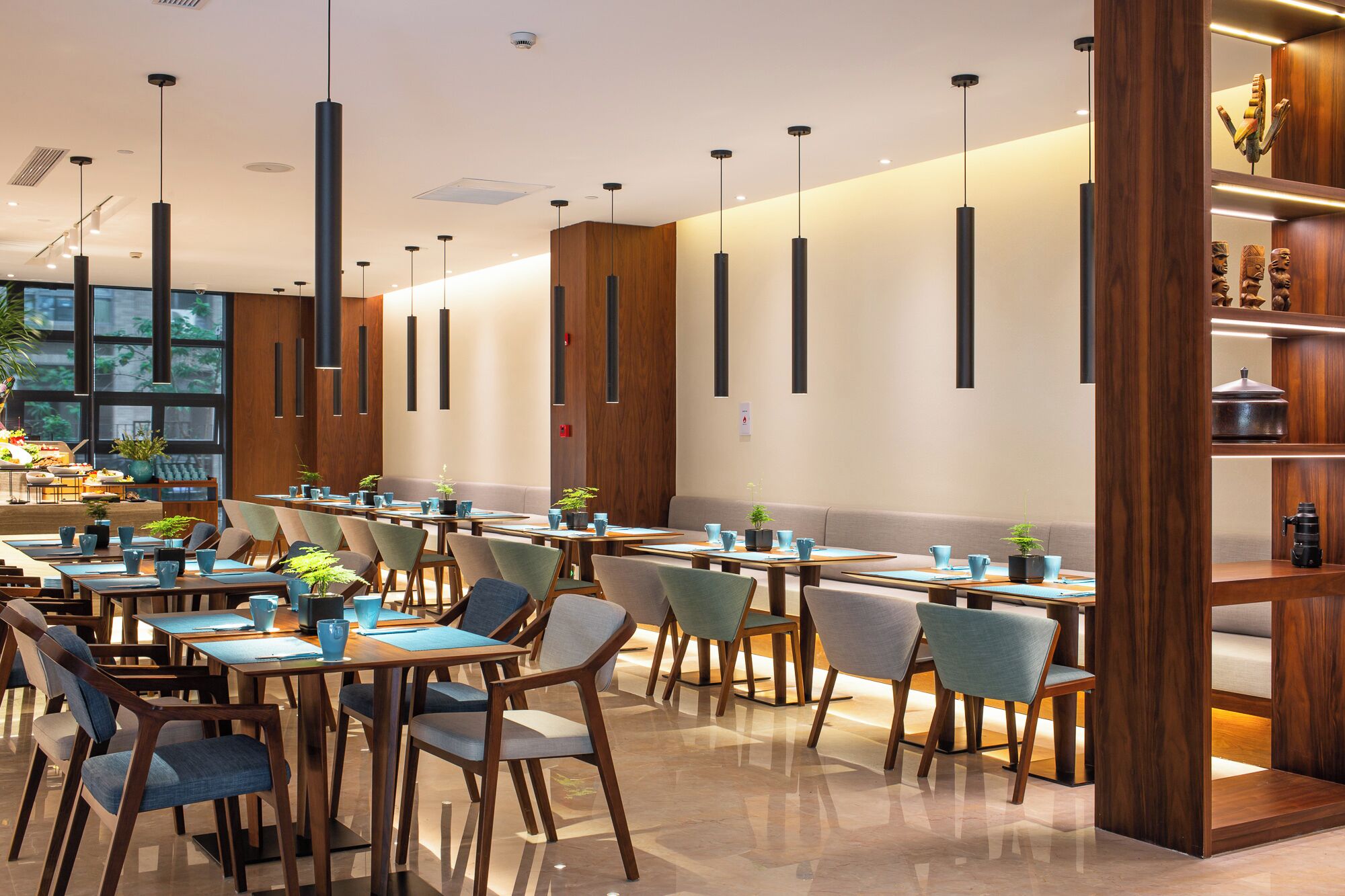 A modern dining area with long tables, chairs, and pendant lighting.