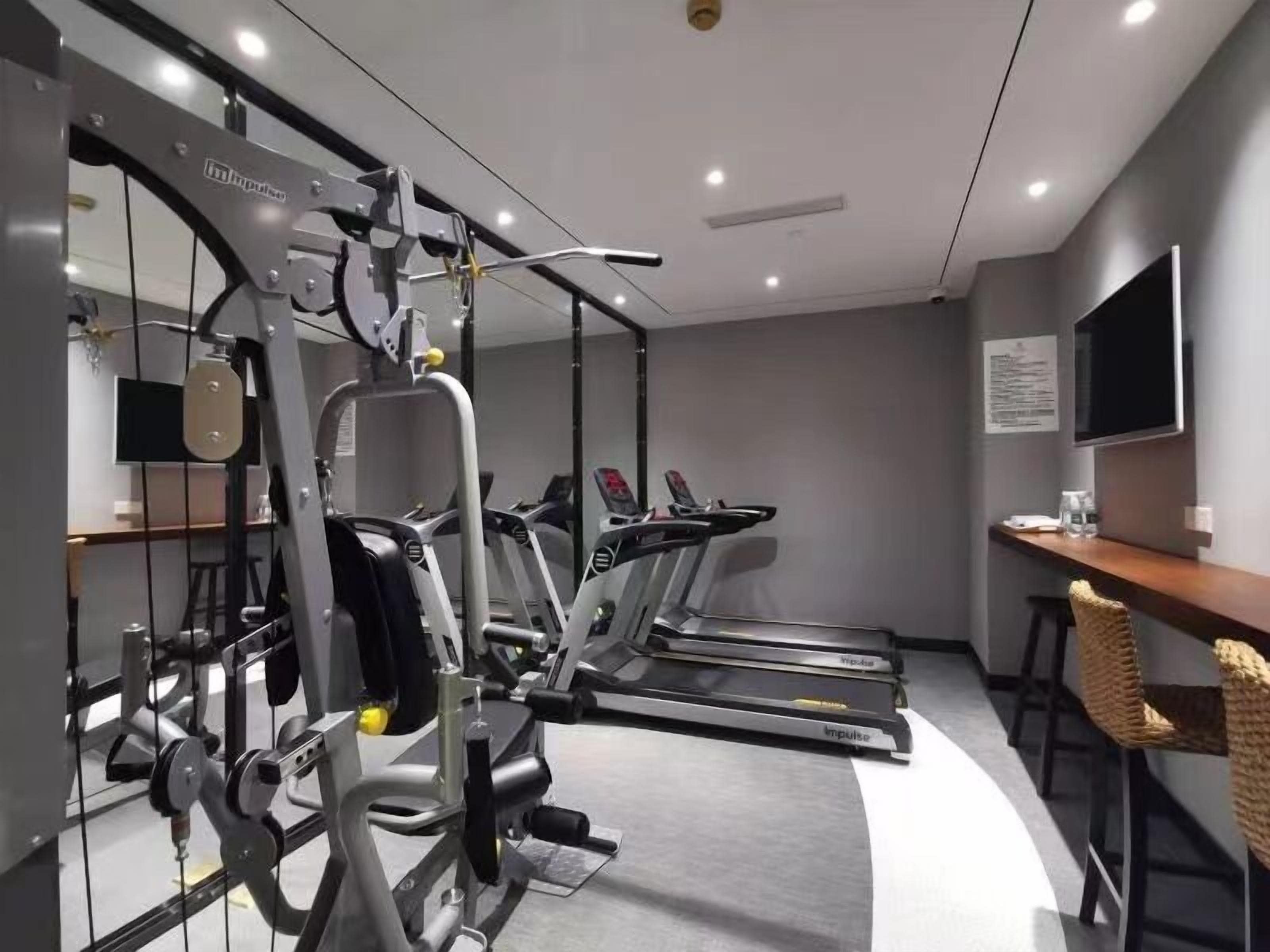 A gym with cardio machines, weight training equipment, and a TV on the wall.