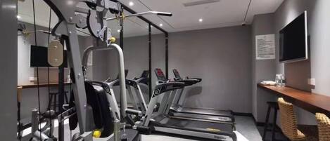 Un gimnasio con máquinas de cardio, equipo de entrenamiento de pesas y un televisor en la pared.