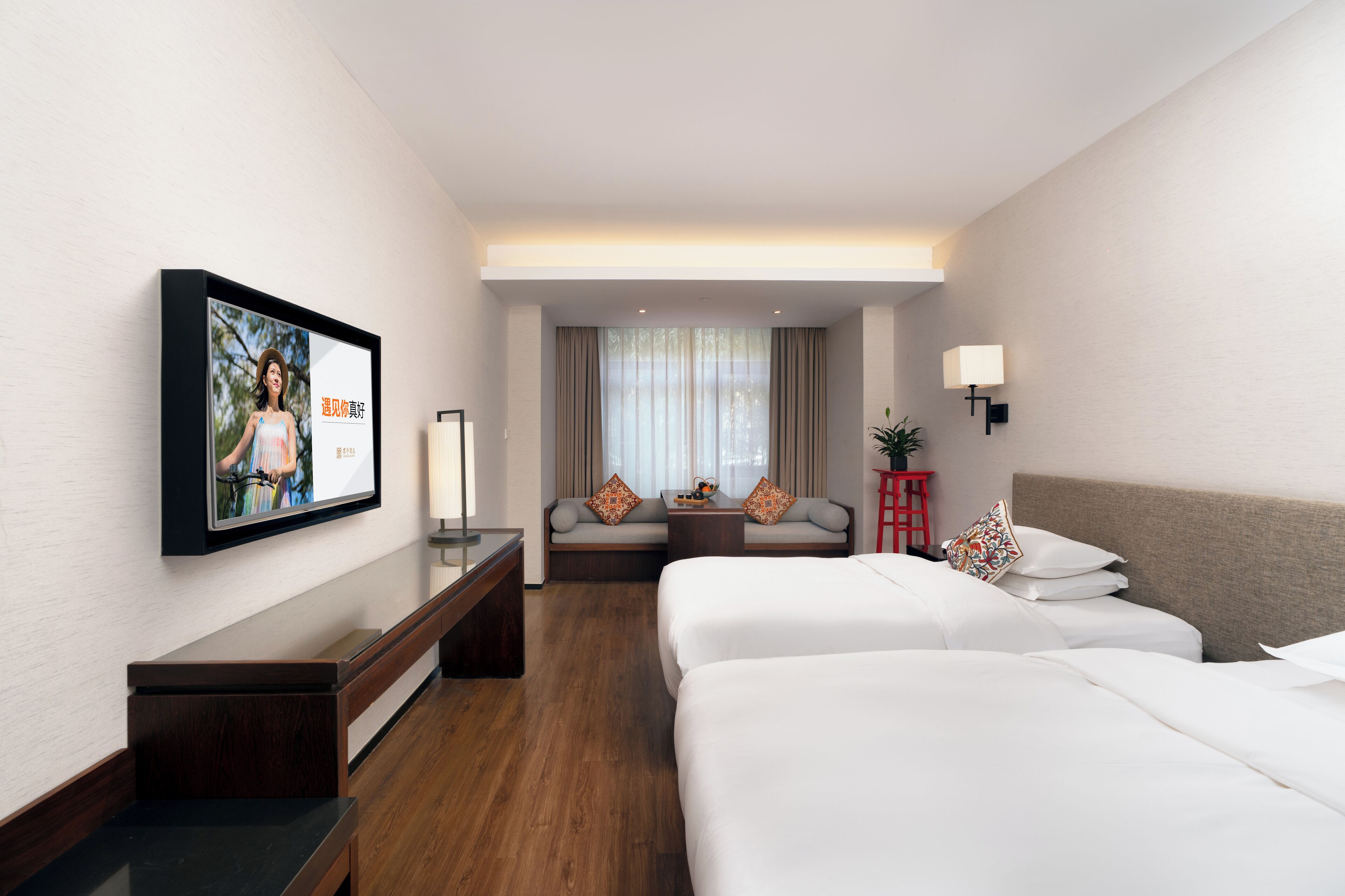 A hotel room with a large bed, a sofa, a TV mounted on the wall, a small table, and a red side table.