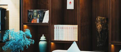A cozy reading nook with a wooden bookshelf filled with books, a comfortable sofa, and a small table with a vase of flowers.
