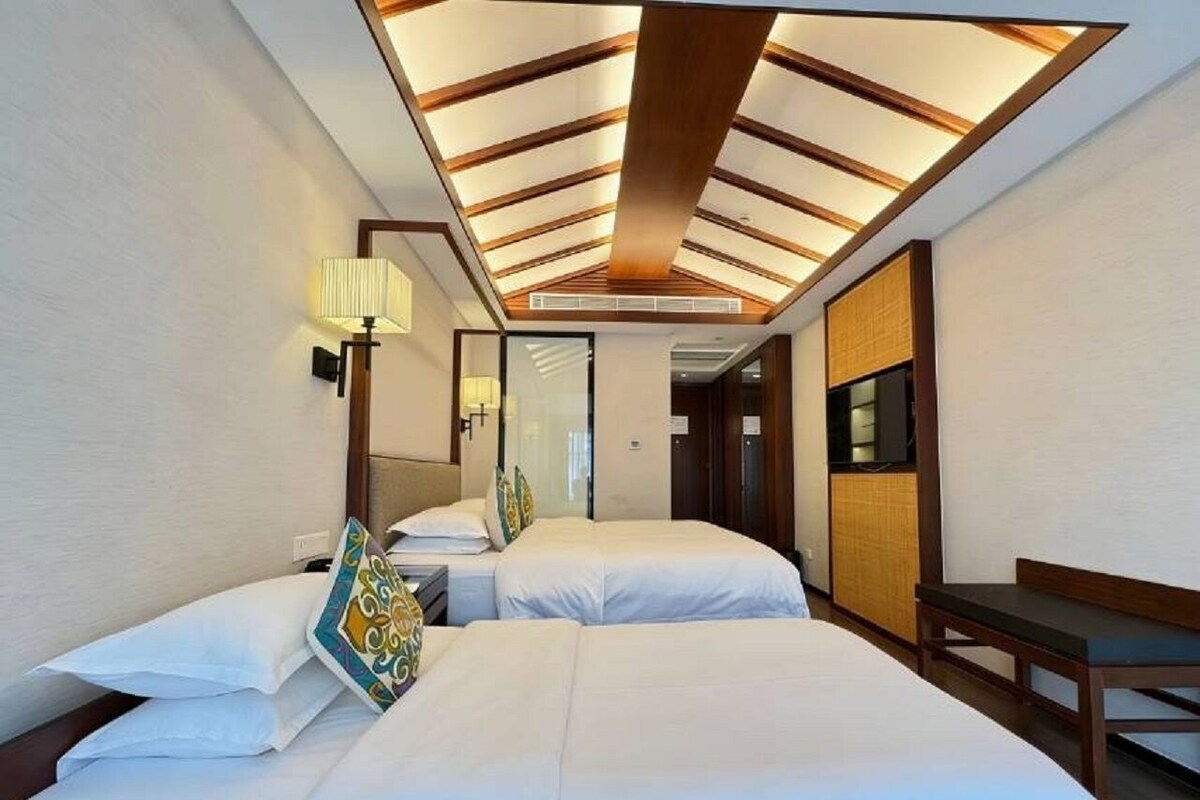 A hotel room with two beds, a desk, a mirror, and a ceiling with wooden beams.