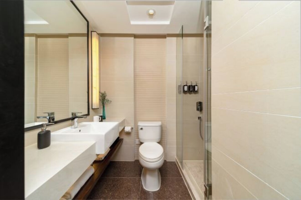 A modern bathroom with a glass shower enclosure, a white toilet, and a dual vanity with a mirror.