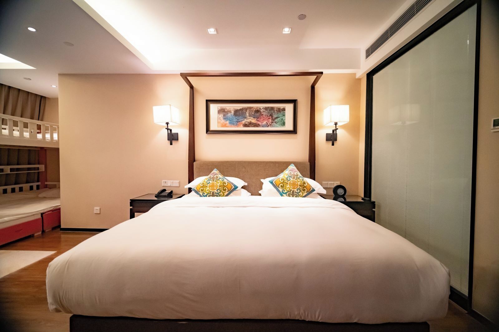 A hotel room with a large bed, two bedside tables, a wall-mounted painting, and two wall-mounted lamps.