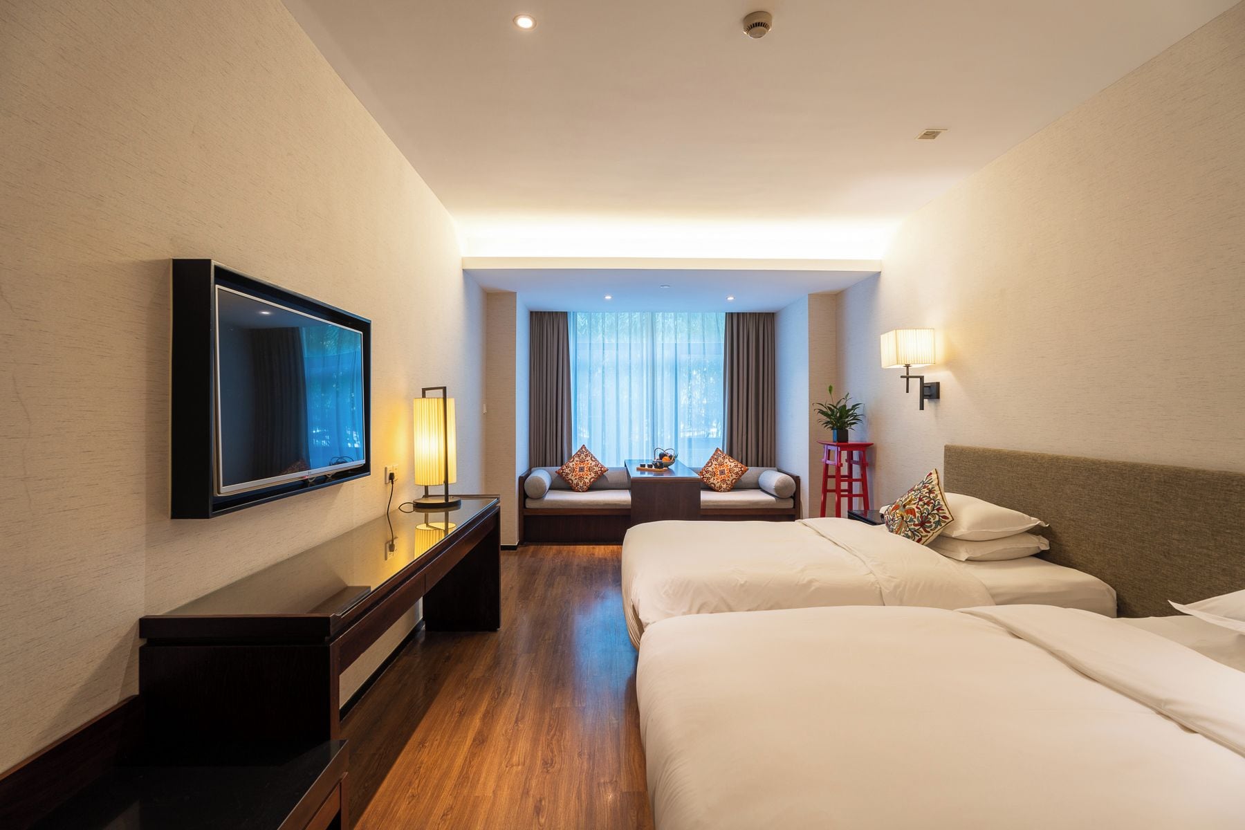 A hotel room with a TV, bedside tables, a sofa, and a bed.