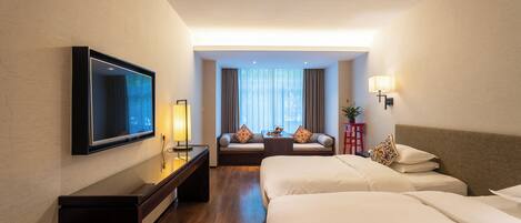 A hotel room with a TV, bedside tables, a sofa, and a bed.
