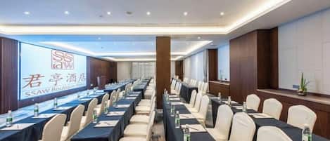 Un salón de conferencias con mesas largas, sillas y una pantalla grande que muestra el logo del Hotel SSAW Boutique.
