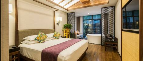 A modern hotel room with a large bed, a small sofa, a private bathroom, and a view of the city.