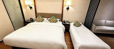 A hotel room with a large bed, a smaller bed, a bedside table with a lamp, and a sofa.