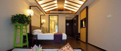 A hotel room with a skylight, a bed with a purple blanket, a green plant, and a sofa with patterned cushions.