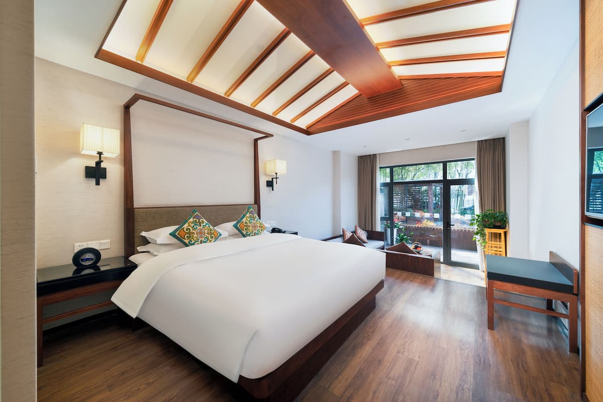 Une chambre d’hôtel moderne dotée d’un grand lit, de poutres apparentes en bois au plafond, d’un bureau et offrant une vue sur l’extérieur.