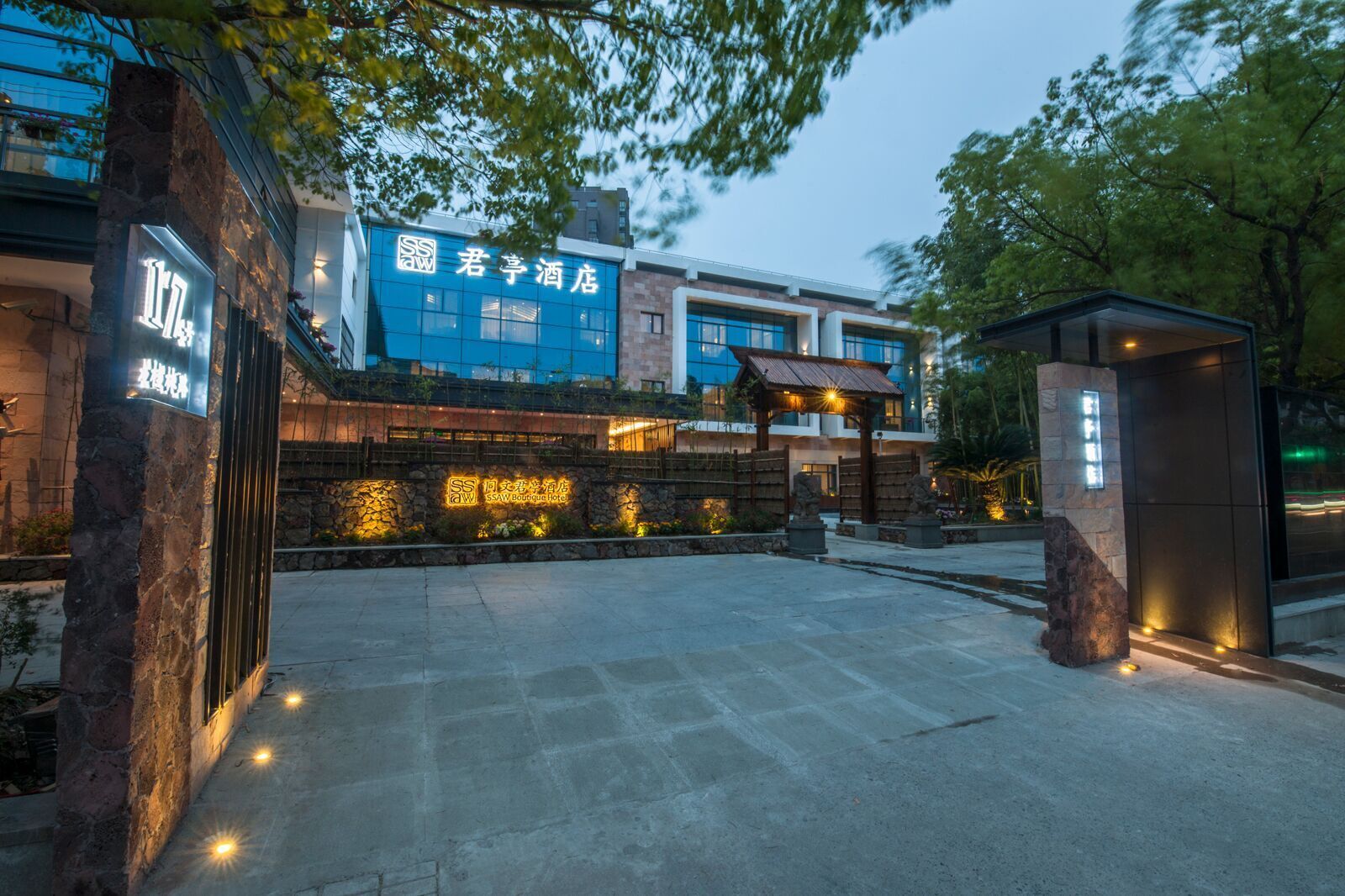 A hotel entrance with a stone wall, illuminated signage, and a modern building in the background.