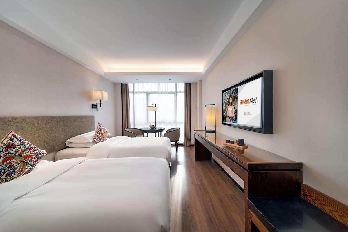 Une chambre d’hôtel avec deux lits, un bureau, une chaise, une télévision et une fenêtre avec des rideaux.