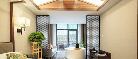 A modern hotel room with a skylight, a large bed, a sitting area with a bathtub, and a view of the outside.