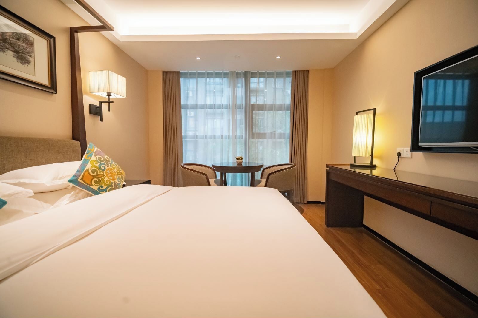 Habitación de hotel con una cama grande, un escritorio, una silla, un televisor y una ventana con cortinas.