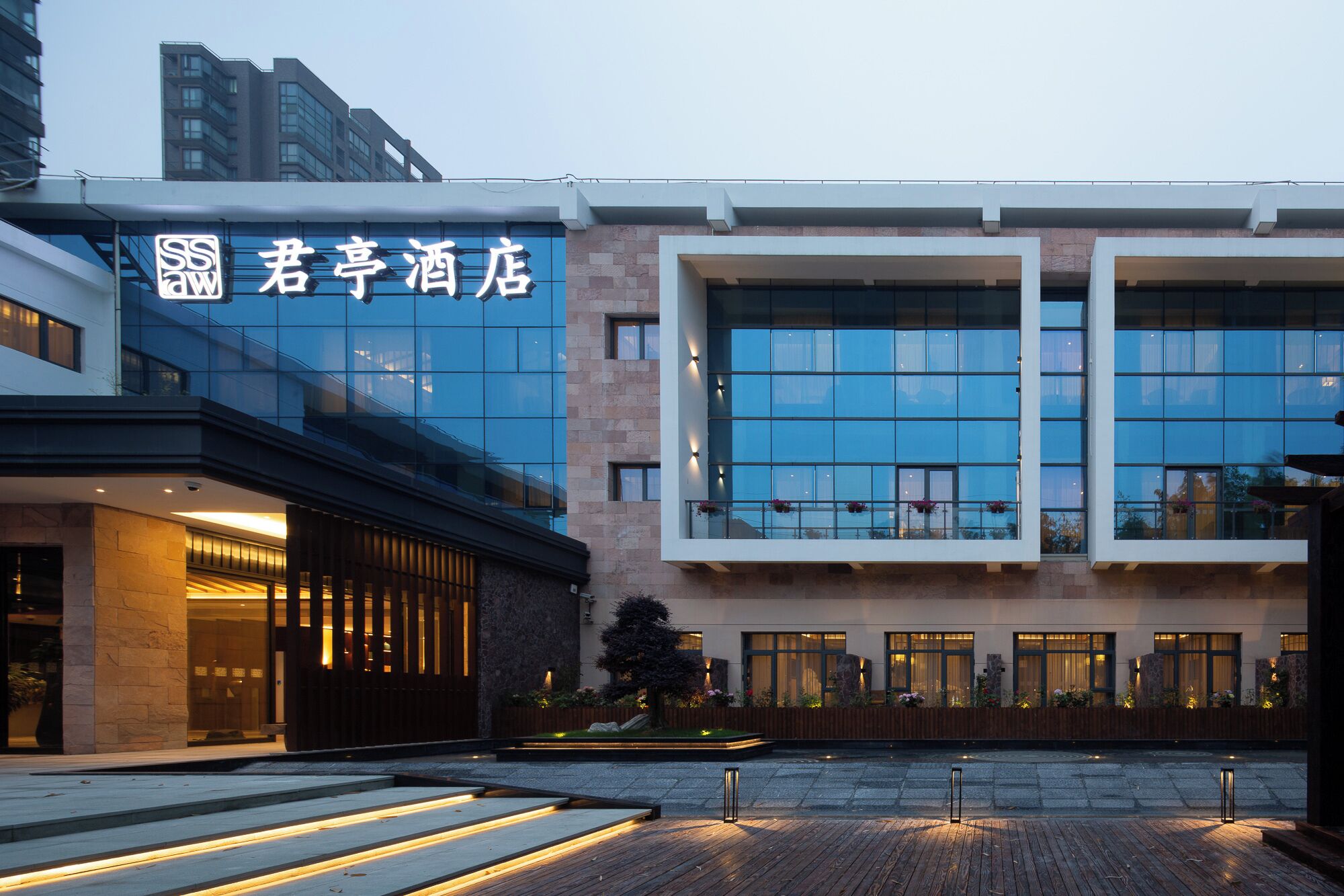 A modern hotel with a glass facade, a wooden deck, and a stone pathway.