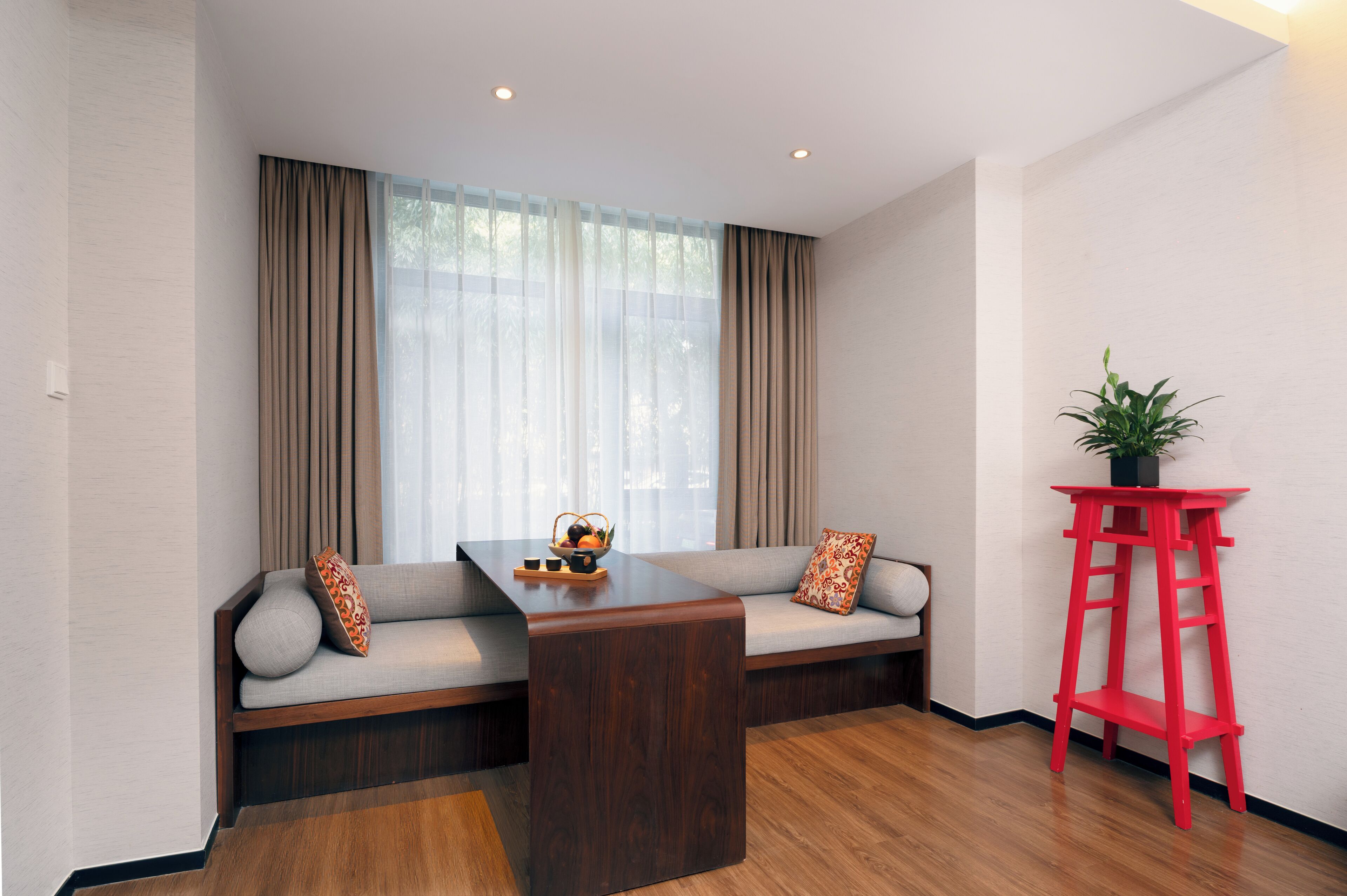 A modern living room with a sofa, a wooden coffee table, and a red side table with a plant.