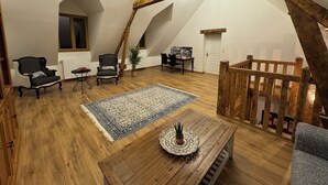 A loft-style room with a wooden ceiling, a blue patterned rug, a wooden coffee table with a plant, and a gray sofa. - Gîte l'orée de Clénord (Mont-près-Chambord)