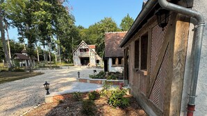 A rustic building with a stone foundation and a wooden facade, a gravel driveway, and a small garden area with plants and a pathway. - Gîte l'orée de Clénord (Mont-près-Chambord)