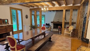 A spacious dining area with a long wooden table, red upholstered chairs, and a fireplace. - Gîte l'orée de Clénord (Mont-près-Chambord)