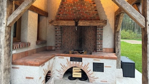 A brick-built outdoor kitchen with a chimney, wooden beams, and a brick hearth. - Gîte l'orée de Clénord (Mont-près-Chambord)