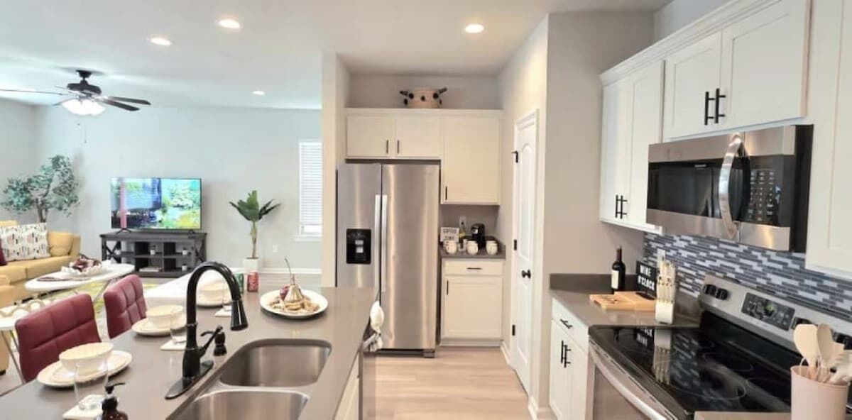 A modern kitchen with stainless steel appliances, a dining area with a sofa and table, and a living room with a TV and seating.