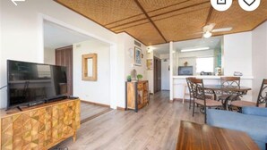 A living room with a TV on a cabinet, a dining area with chairs and a table, and a kitchen in the background. - Charming 2-bedroom apartment in Honolulu with AC, WiFi parking (Honolulu)