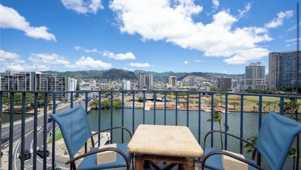 A balcony with two chairs and a small table, overlooking a cityscape with buildings and a river. - Charming 2-bedroom apartment in Honolulu with AC, WiFi parking (Honolulu)