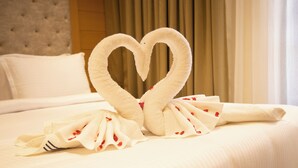Una cama bien hecha con una disposición de toallas en forma de corazón y una toalla doblada con detalles rojos.