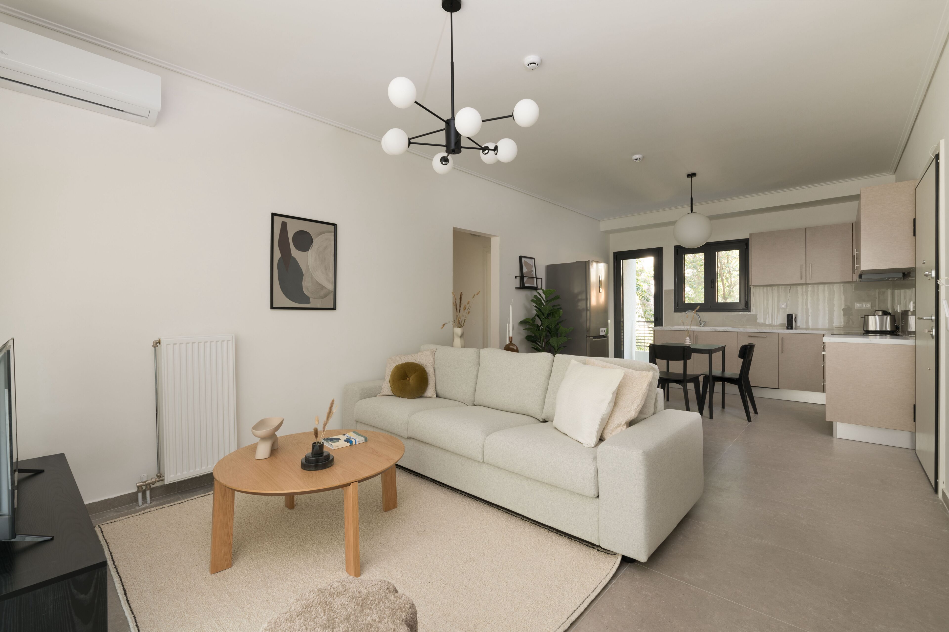 A modern living room with a sofa, coffee table, and TV. There is a kitchen area with cabinets and a dining table.