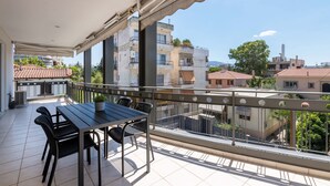 Un balcon avec une table et des chaises, donnant sur un quartier résidentiel avec des immeubles et des arbres.