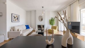 Un salon moderne avec une table à manger en bois foncé, un canapé beige, un fauteuil jaune, un téléviseur et une cheminée.