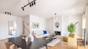 Un salon moderne avec une table à manger en bois foncé, des chaises beiges, un canapé blanc avec un coussin bleu, un fauteuil jaune et une grande plante.