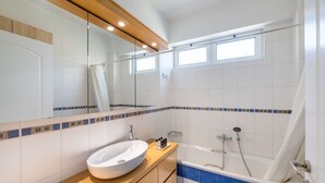Une salle de bain moderne avec un grand miroir, un lavabo blanc, une baignoire et des murs recouverts de carreaux bleus.