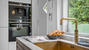 Une cuisine au design moderne, dotée d’un four en acier inoxydable, d’un micro-ondes encastré et d’une grande fenêtre offrant une vue sur la verdure.