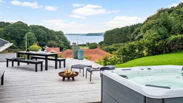 Une terrasse dotée de mobilier d’extérieur, d’un jacuzzi et d’un foyer, le tout offrant une vue sur un lac.