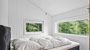 Une chambre à coucher avec un lit, deux fenêtres et une vue sur les arbres.